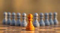 Golden wooden pawn stands out from blurred white and gray pieces on chessboard, symbolizing leadership, strategy, and competitive advantage in business and games.