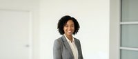 Professional African American businesswoman in gray suit smiling confidently in modern office environment for corporate presentations and marketing materials.