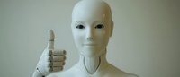 White humanoid robot giving thumbs up gesture against neutral background, showing positive artificial intelligence interaction and future technology concept.