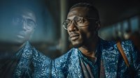 African American businessman in stylish patterned suit and glasses looking confidently ahead in modern office environment with dramatic lighting.