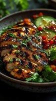 Grilled chicken breast sliced and served with fresh salad, cherry tomatoes, and cucumber in dark ceramic plate. Glazed meat with herbs and spices.