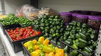 Fresh colorful bell peppers, tomatoes and green beans displayed in plastic containers at grocery store produce section, arranged on metal shelving.