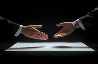 Business partners reaching hands for handshake over contract document on dark background, dramatic lighting emphasizes trust and agreement in professional setting.