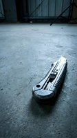 Utility knife lying on concrete floor in industrial warehouse setting with metal shelving in background for construction and renovation projects.