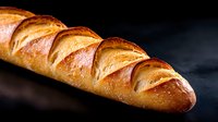 Fresh baked golden French baguette with crispy crust and diagonal scoring marks on dark background, close up view of artisanal bread photography.