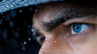 Close up macro shot of intense blue eye with water drops and dark dramatic lighting, showing deep emotion and mystery in artistic portrait photography.
