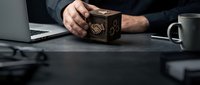 Businessman hands holding wooden cube with handshake symbol at office desk with laptop and coffee mug representing partnership and collaboration concepts.