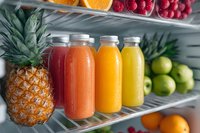 Fresh fruit juices in glass bottles on refrigerator shelf with pineapple, apples, oranges, and berries for healthy lifestyle and detox cleanse.