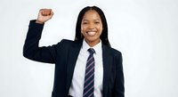Confident African American businesswoman in navy suit celebrating success with raised fist gesture, smiling professionally on white background.
