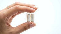 Hand holding two white capsules pills between fingers on clean background for medical healthcare pharmaceutical supplement concept.