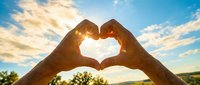 Hands forming heart shape against bright sunset sky with golden sunlight streaming through fingers creating romantic silhouette for love and connection concepts.
