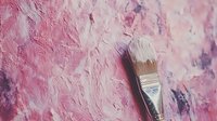 Paint brush lying on pink and purple textured acrylic paint background with thick impasto strokes, creating artistic composition for creative design projects.