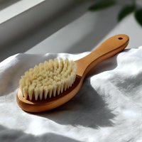 Natural wooden massage brush with soft bristles on white textile background, minimalist spa and wellness composition for body care and relaxation.