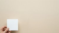 Hand holding blank white card or paper against neutral beige background, suitable for mockups, branding, and business presentations.