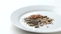Assorted healthy seeds and nuts including chia, pumpkin, sunflower seeds arranged on white ceramic plate for nutritious snacking and cooking.