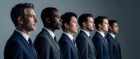 Diverse group of professional businessmen in suits standing in profile formation against gray background for corporate teamwork concepts.