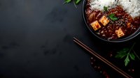 Spicy mapo tofu with steamed rice in a dark bowl, garnished with sesame seeds and parsley, served with chopsticks on a black stone surface.