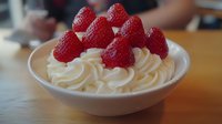 Fresh raspberries topped on swirled whipped cream in white bowl on wooden table. Delicious dessert ready for serving in cozy kitchen setting.