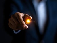 Businessman holding glowing light spark between fingers against dark background, representing innovation, creativity and business vision concept.