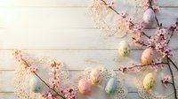 Easter eggs with blooming cherry branches and lace decorations on white wooden background. Spring holiday celebration concept with pastel colored eggs.