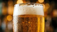 Chilled beer glass with golden lager and thick foam head, condensation droplets on exterior, warm bokeh background, suitable for beverage advertising and hospitality marketing.