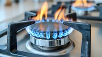 Gas stove burner with blue and orange flames on modern kitchen cooktop. Close-up view of natural gas cooking appliance with metal grate and control knobs.