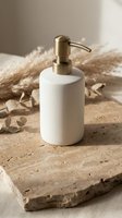 Elegant white ceramic soap dispenser with brass pump on natural stone surface surrounded by dried pampas grass and eucalyptus for modern bathroom decor.