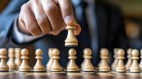 Close-up of hand moving white wooden pawn chess piece above row of pawns on wooden surface, demonstrating leadership and strategic business decision making concept.