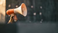 Hand holding red and white megaphone against blurred background for communication, announcement, marketing campaigns and public speaking concepts.