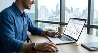 Professional businessman working on laptop computer in modern office with city skyline view. Corporate executive analyzing data and reports at desk.