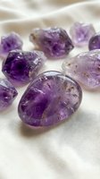 Raw amethyst crystals and tumbled stones arranged on soft white fabric for healing meditation and spiritual wellness practices.