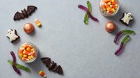 Halloween candy corn, chocolate bats, ghost cookies and gummy worms arranged on gray background for autumn holiday celebration and trick or treat festivities.