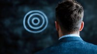 Caucasian man in business attire looking at glowing blue circular target pattern against dark background. Concept of focus, goals and achievement in business.