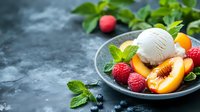 Fresh summer dessert with vanilla ice cream scoop, sliced peach, raspberries, blueberries and mint leaves on dark plate against moody background. Food styling.