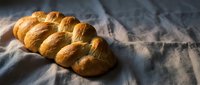 Golden braided challah bread loaf on linen cloth with dramatic lighting and shadows for bakery, cooking, and food photography projects.
