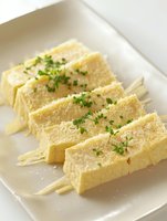 Fresh egg sandwich triangles garnished with chopped herbs and served on white plate, soft focus close up view of classic tea party finger food.