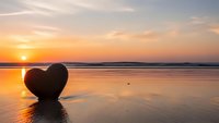 Heart-shaped stone on tranquil beach at golden sunset with calm ocean waves and romantic sky reflection creating peaceful seascape for love concepts.