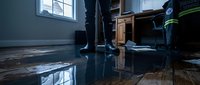 Flooded home interior with water damage on hardwood floors reflecting window light creating emergency restoration scene for insurance claims.