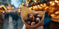Roasted chestnuts in paper cone at festive Christmas market with blurred lights and crowd in background, traditional winter holiday street food.