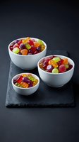 Colorful assorted gummy candies in white ceramic bowls on dark slate board, sweet treats for parties and celebrations.