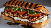 Grilled chicken sandwich with fresh mozzarella, tomatoes, and arugula on toasted brioche bun, drizzled with balsamic glaze. Close-up food photography.