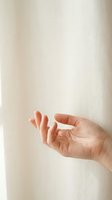 Close-up of a Caucasian hand with fingers gently curved in a graceful gesture against soft white linen curtain background.