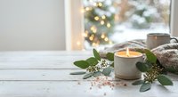 Cozy winter morning scene with steaming coffee mug, eucalyptus leaves and warm blanket by window with Christmas tree lights creating peaceful holiday atmosphere.