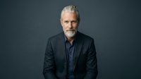 Mature man with gray hair and beard wearing dark blazer and blue shirt against neutral background, suitable for corporate portraits and professional headshots.