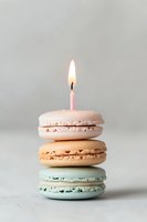 Stack of colorful macarons with lit birthday candle on neutral background for celebration and party concepts.