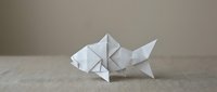 White origami fish crafted from folded paper, displayed on a neutral linen surface against a soft beige background, showcasing Japanese art.