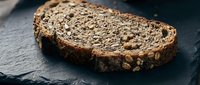 Artisan whole grain bread slice with seeds and nuts on dark slate surface for healthy eating and bakery concepts.