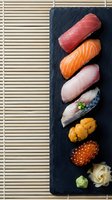 Assorted nigiri sushi pieces arranged vertically on black slate with bamboo placemat, featuring tuna, salmon, squid, scallop, sea urchin and salmon roe for restaurant menus and culinary content.