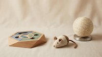 Wooden cat puzzle toy, knitted mouse, and sisal scratching ball on neutral fabric background, eco-friendly pet accessories for cats.