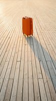 Orange hardshell suitcase standing alone on a wooden boardwalk with a long shadow, evoking travel, adventure, and departure.
